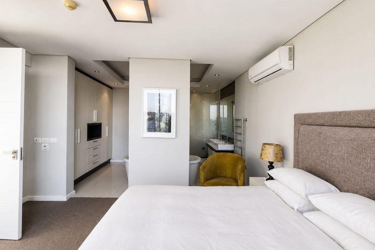 Spacious bedroom featuring built-in cupboards, split-system air conditioning, and an open-plan en-suite bathroom with a double vanity and freestanding bathtub.
