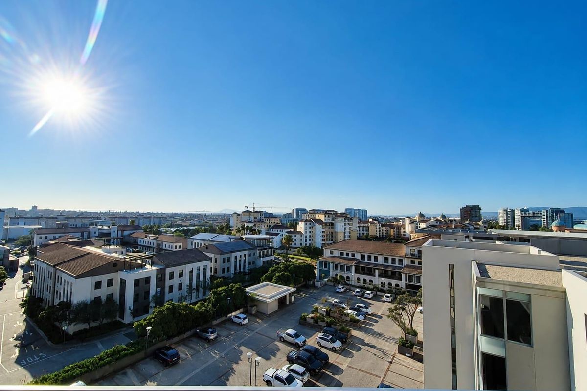 Elevated urban view overlooking a residential complex and parking area, captured from a balcony with a modern glass balustrade.