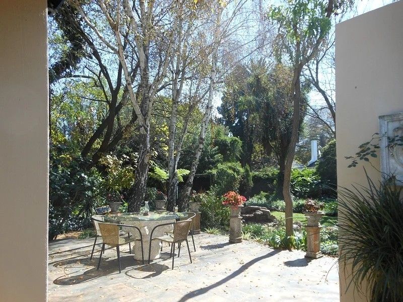 A paved outdoor patio area overlooking a lush, mature garden with established trees and stone decorative features.
