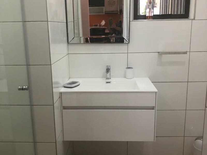 A modern bathroom featuring a wall-mounted vanity with a white basin, large format wall tiles, and a framed mirror.