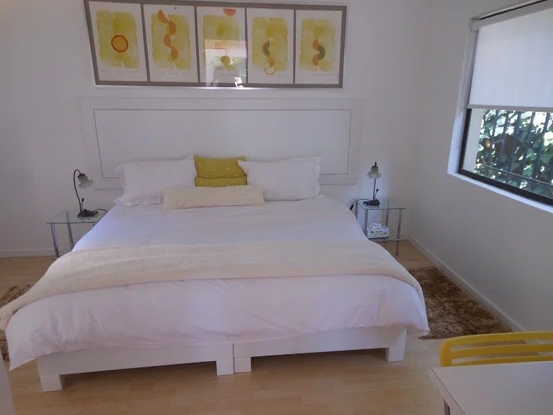 A bright and well-maintained bedroom featuring light wood-look flooring, a built-in headboard, and a window with a roller blind.