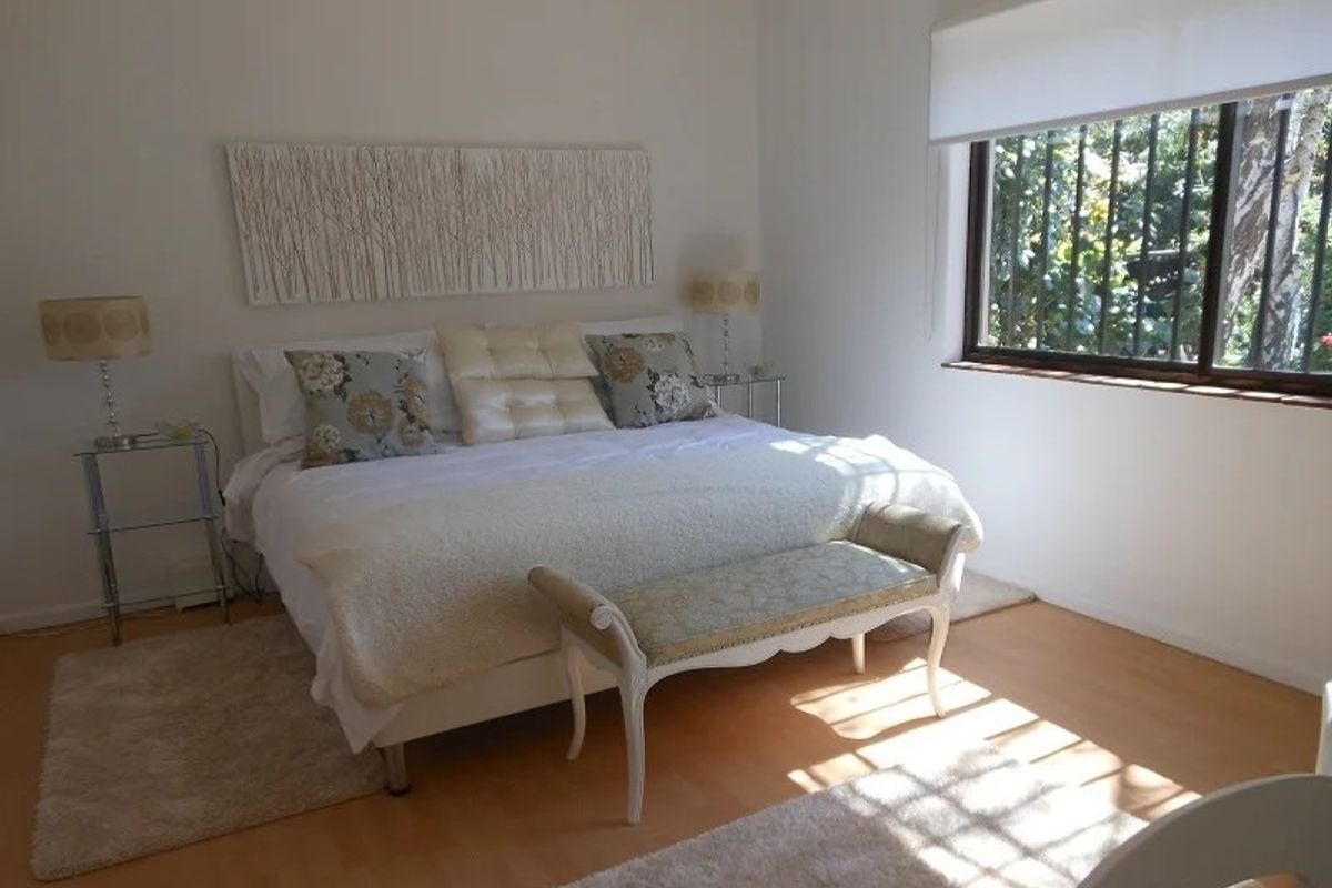 A bright bedroom featuring light wood-look flooring, a large window with security bars, and neutral wall finishes.