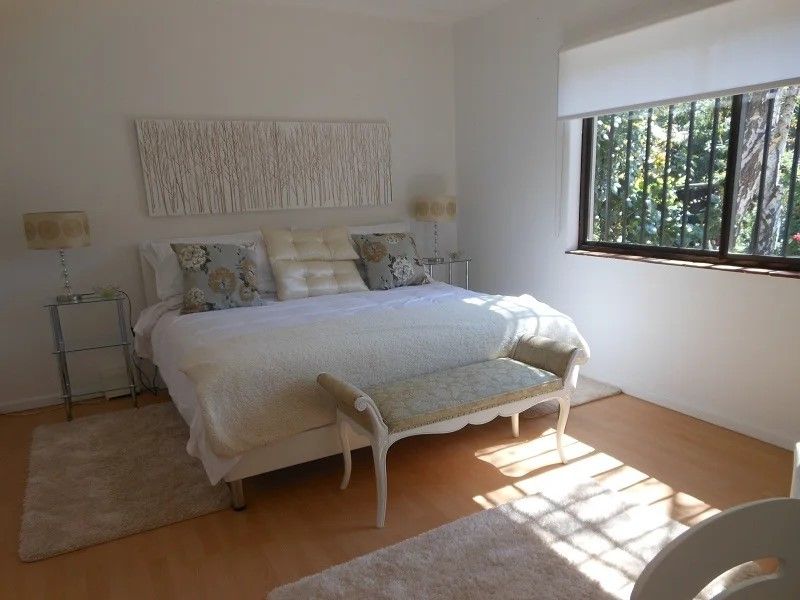 A bright bedroom featuring light wood-look flooring, a large window with security bars, and neutral wall finishes.