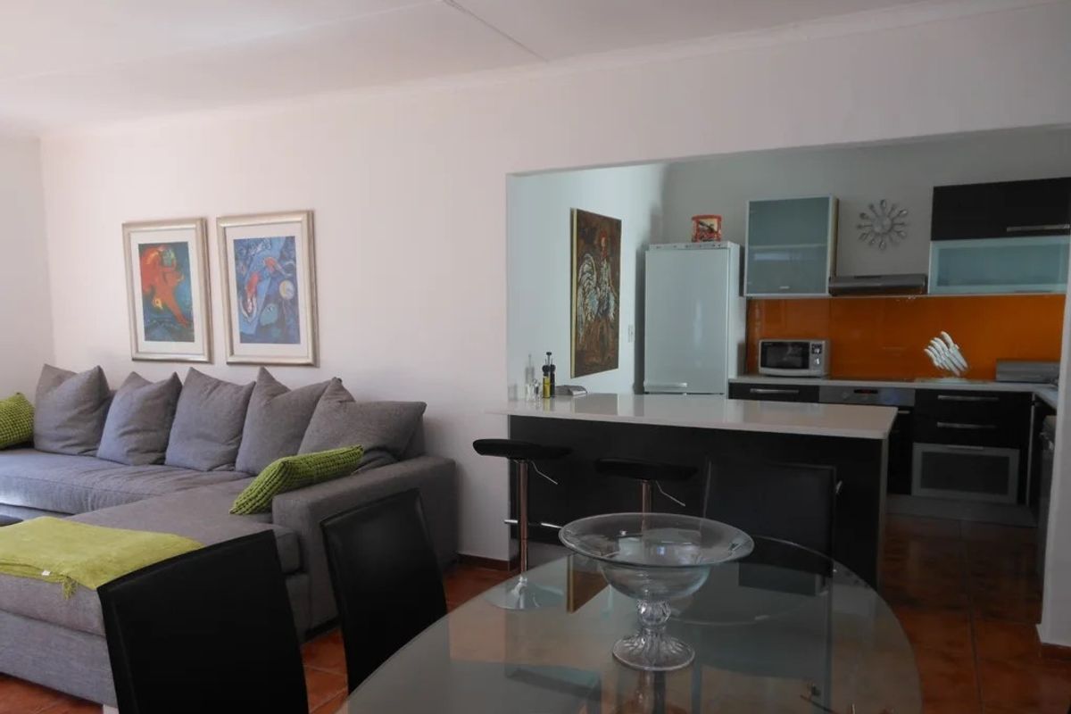 Open-plan living and dining area featuring a modern kitchen with a breakfast bar, sleek cabinetry, and a vibrant orange glass splashback.