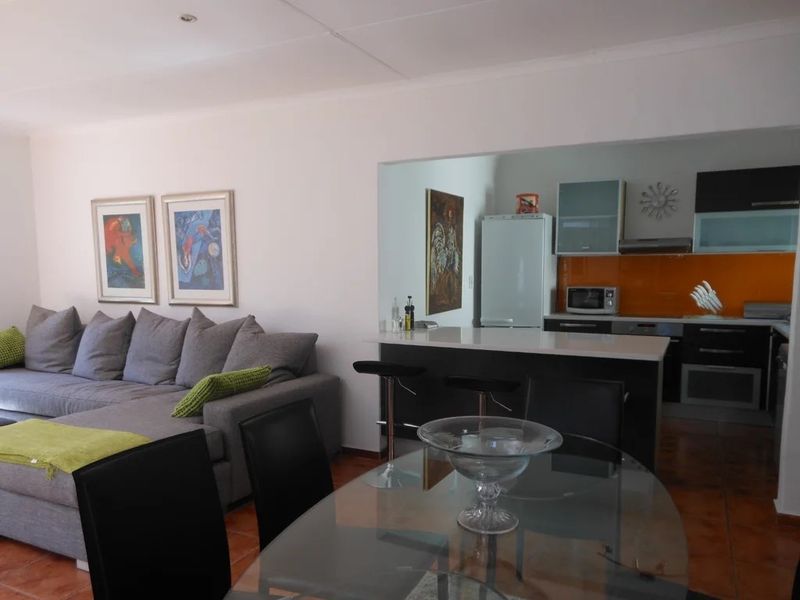 Open-plan living and dining area featuring a modern kitchen with a breakfast bar, sleek cabinetry, and a vibrant orange glass splashback.
