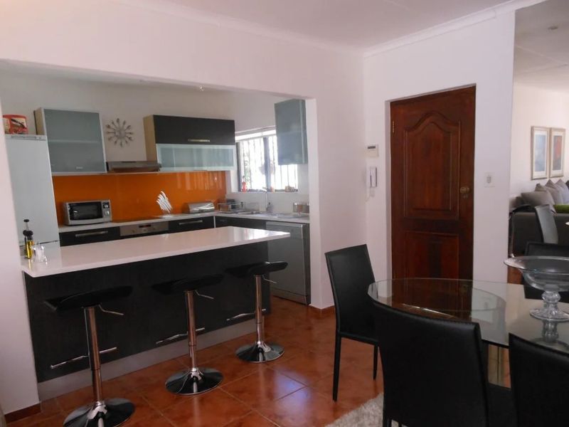 Open plan kitchen featuring a breakfast bar, modern cabinetry, and a vibrant orange glass splashback, seamlessly connecting to the dining area.