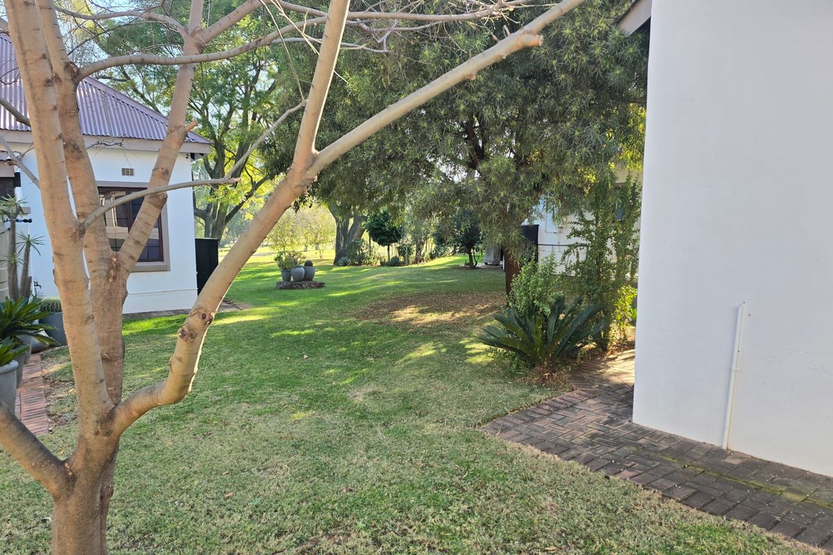 A view of the spacious rear garden area featuring established trees, manicured lawn, and paved pathways between the townhouse structures.