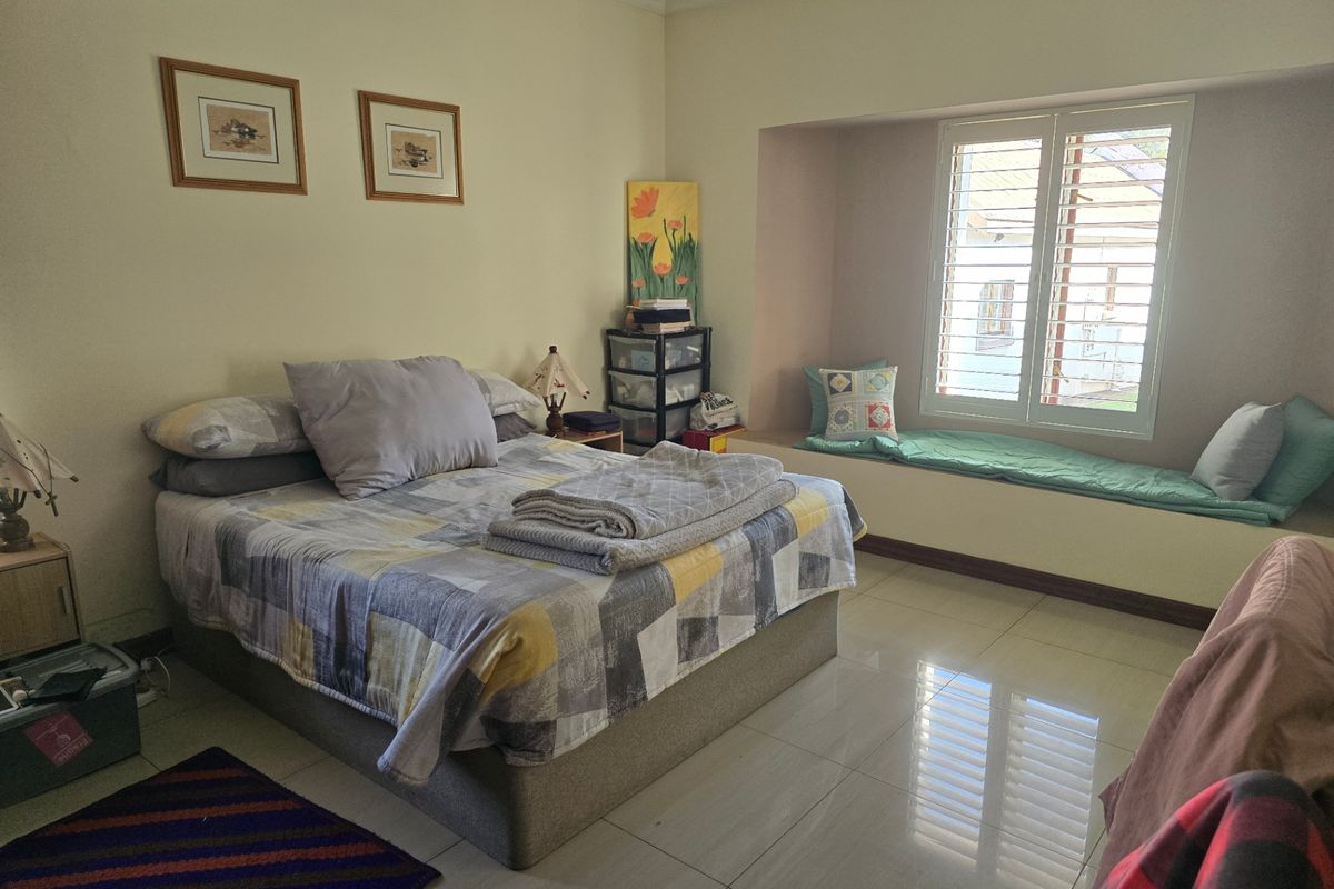 A bedroom featuring large format floor tiles, a built-in window seat with plantation shutters, and crown molding.