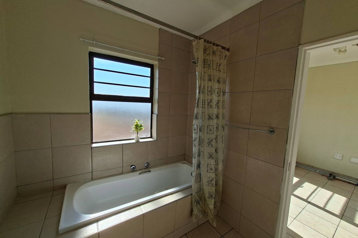 A functional bathroom featuring a built-in bathtub with shower attachment, tiled walls, and a window providing natural light.