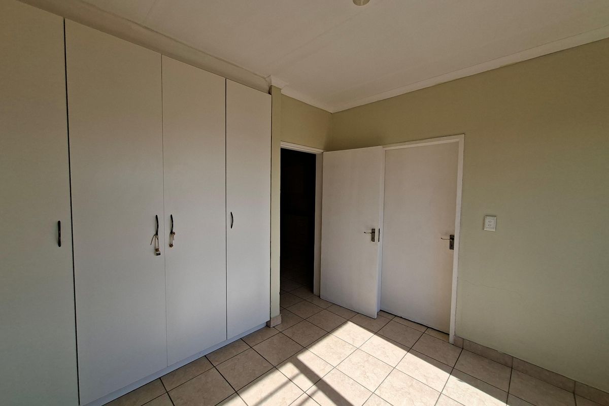 A bedroom featuring built-in cupboards, tiled flooring, and neutral wall finishes, offering a functional and clean living space.
