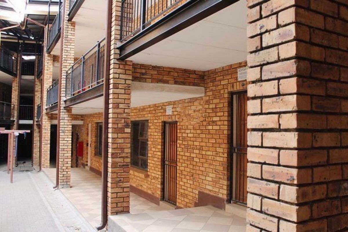 Exterior view of an apartment complex featuring multi-level walkways, exposed brick facade, metal railings, and tiled flooring.