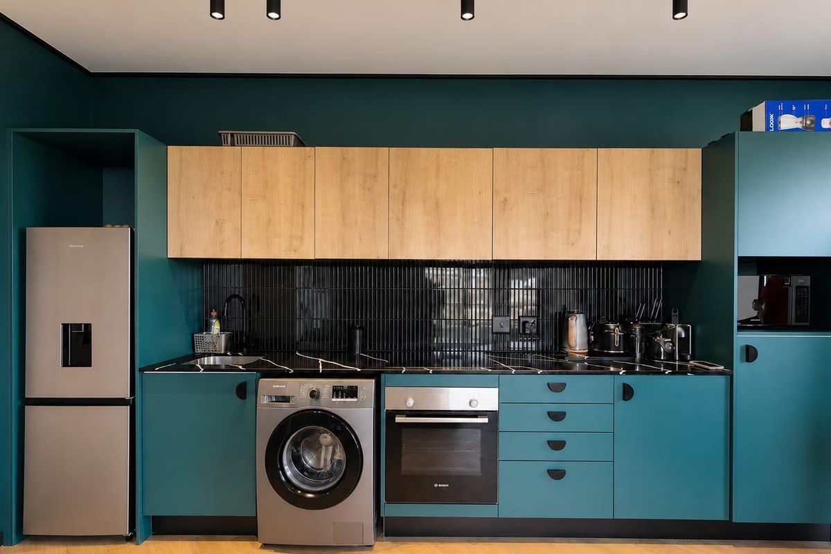 Modern kitchen featuring teal and wood-tone cabinetry, black marble-effect countertops, black subway tile backsplash, and integrated appliances with contemporary track lighting.