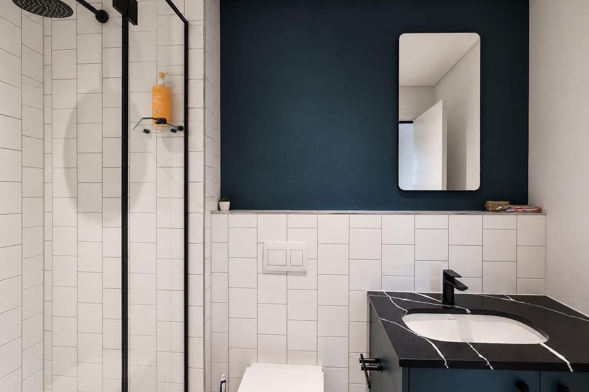 Modern bathroom featuring a walk-in shower with black fixtures, a wall-mounted toilet, and a vanity unit with a marble-effect countertop.