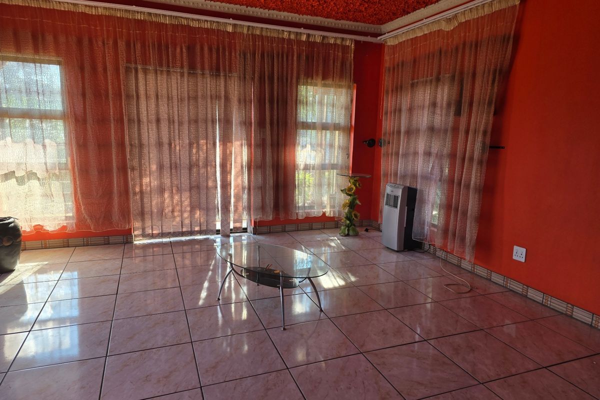A living room featuring large windows with sheer curtains, tiled flooring, and a textured ceiling finish.
