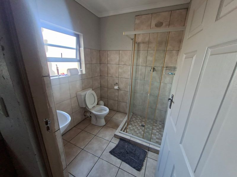 A functional bathroom featuring a glass-enclosed shower, ceramic floor and wall tiling, a standard toilet, and a basin.