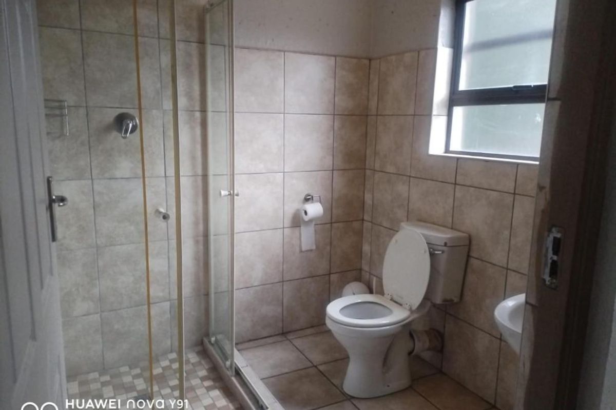 A functional bathroom featuring a glass-enclosed shower, a standard toilet, and tiled walls and flooring.