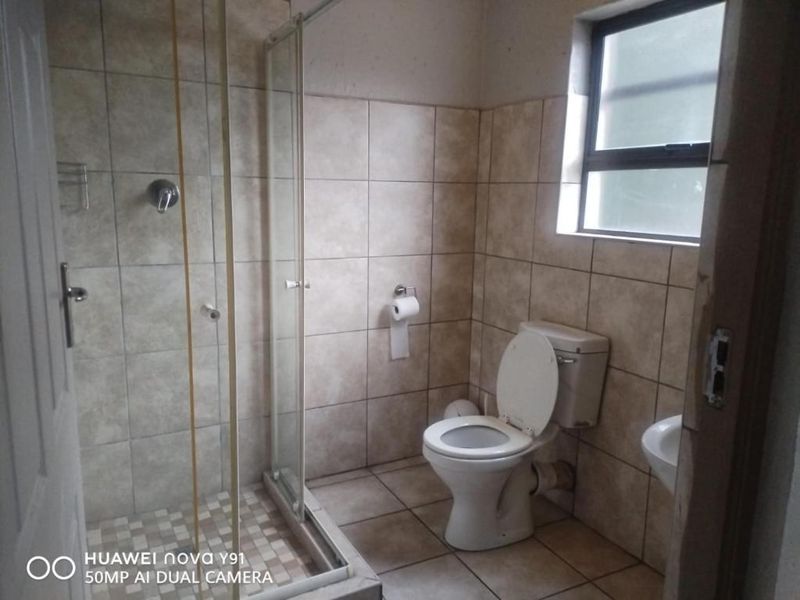 A functional bathroom featuring a glass-enclosed shower, a standard toilet, and tiled walls and flooring.