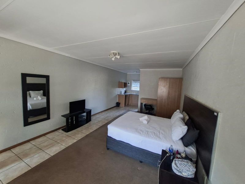 A spacious open-plan studio unit featuring a sleeping area with carpet flooring, a small kitchenette, and tiled flooring in the entrance and kitchen zone.