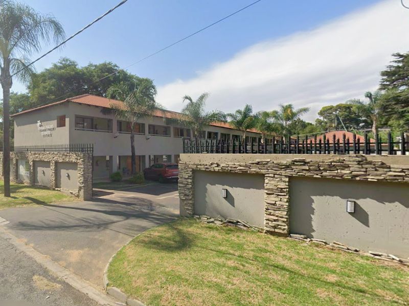 Street view of a commercial property complex featuring a paved entrance, perimeter stone-clad boundary walls, and multi-level building structure.