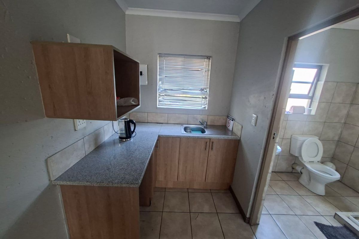 A functional scullery area featuring built-in cabinetry, a granite-look countertop, and a stainless steel sink, with an adjacent bathroom visible.