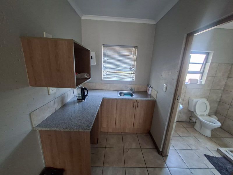 A functional scullery area featuring built-in cabinetry, a granite-look countertop, and a stainless steel sink, with an adjacent bathroom visible.