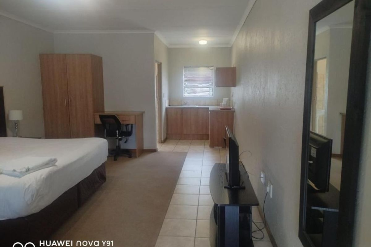 A studio-style bedroom featuring a kitchenette area with built-in cabinetry, tiled flooring, and a carpeted sleeping zone.