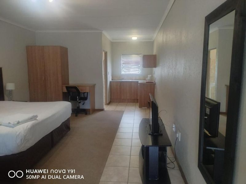 A studio-style bedroom featuring a kitchenette area with built-in cabinetry, tiled flooring, and a carpeted sleeping zone.
