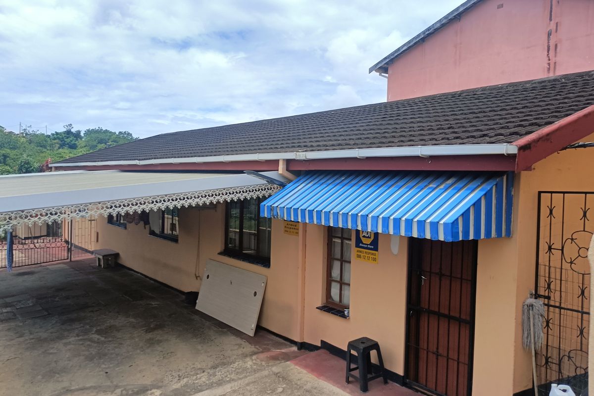 Rear exterior view of the house featuring a tiled roof, metal carport, and a security gate with a striped fabric awning.