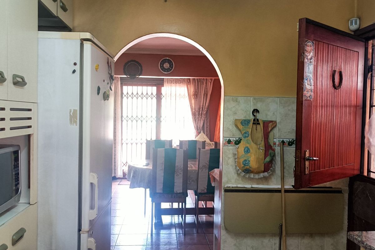 A dated kitchen featuring tiled splashbacks and an arched doorway leading to the dining area, with potential for modern cosmetic updates.
