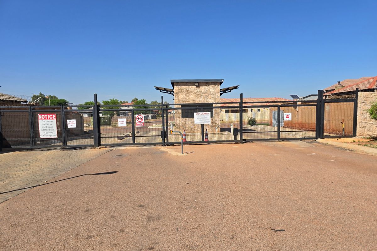 A secure gated entrance to a residential estate featuring a stone-clad guardhouse, metal security fencing, and controlled access points.