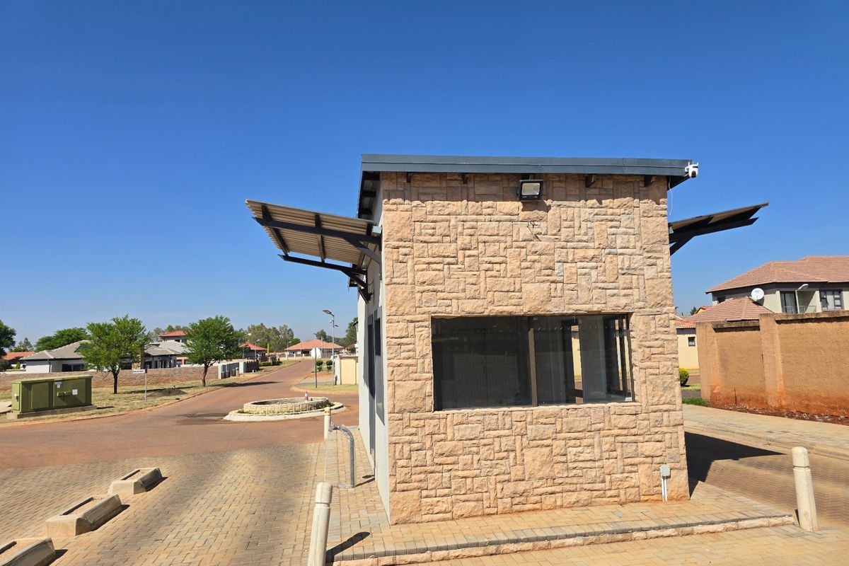 A secure guardhouse structure featuring stone cladding, metal roofing, and large windows, situated at the entrance of a residential estate.