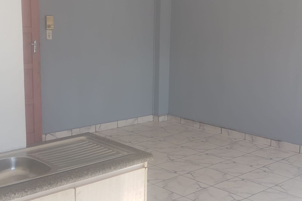 An empty kitchen area featuring a stainless steel sink, tiled flooring, and neutral grey walls, providing a blank canvas for potential updates.
