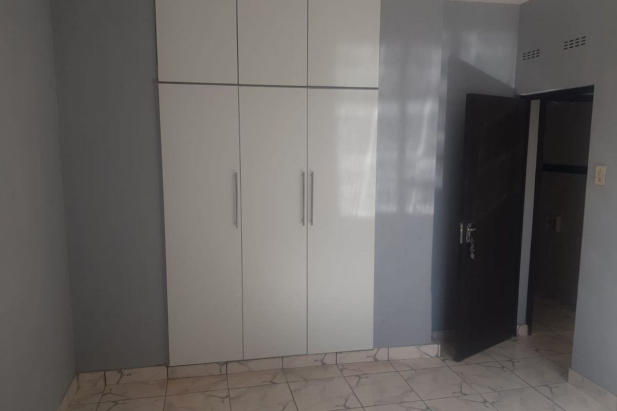 A bedroom featuring built-in floor-to-ceiling white cabinetry, tiled flooring, and a dark interior door leading to an adjacent space.