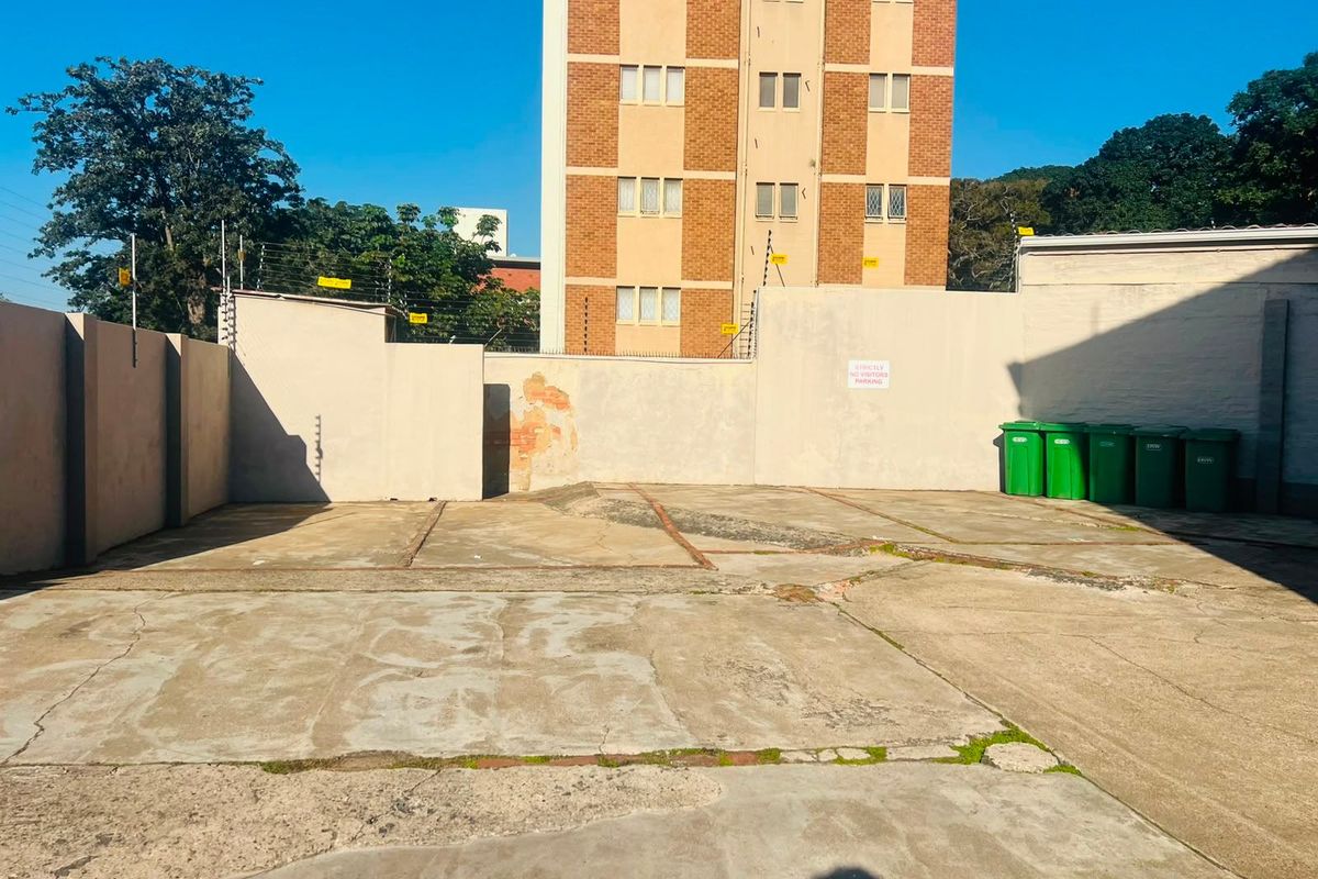 An outdoor parking or utility area featuring concrete paving, perimeter boundary walls with electric fencing, and a view of the adjacent apartment building.