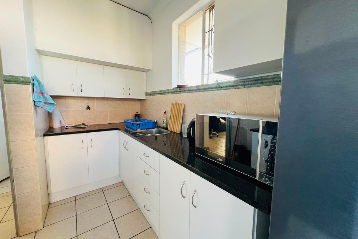 A functional kitchen featuring white cabinetry, dark granite countertops, tiled splashbacks, and a built-in microwave space, offering a clean and practical layout.