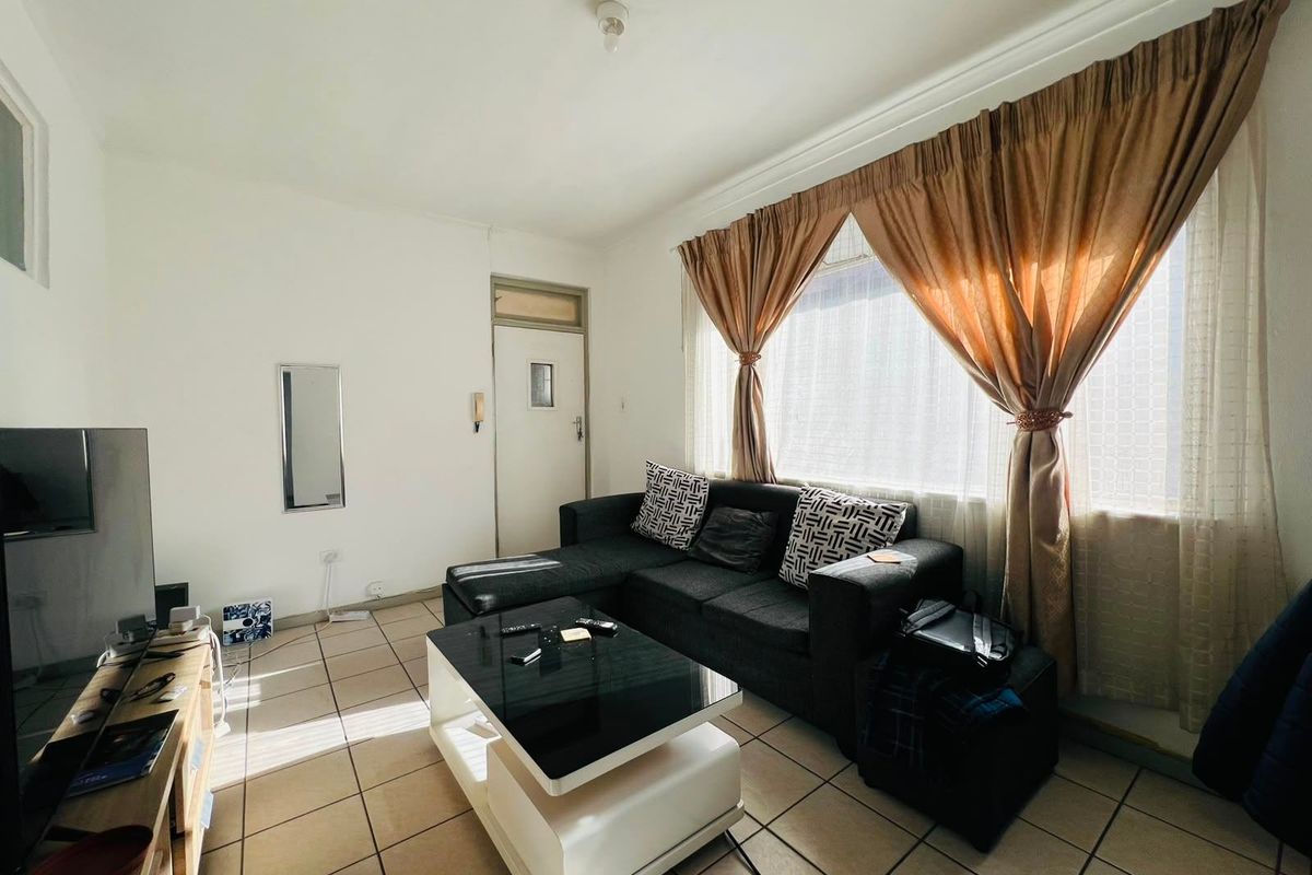 A living room featuring tiled flooring and a large window with curtains, providing a functional and well-lit space.