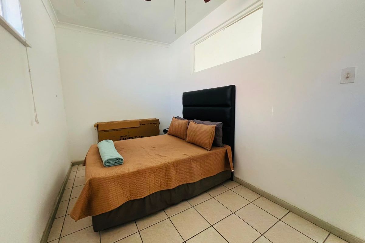 A compact bedroom featuring tiled flooring, a ceiling fan, and high-set windows providing natural light.