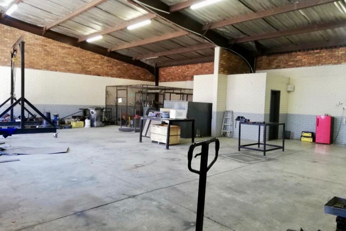 Spacious industrial utility area featuring exposed steel roof trusses, durable concrete flooring, and brick masonry walls, suitable for workshop or storage operations.