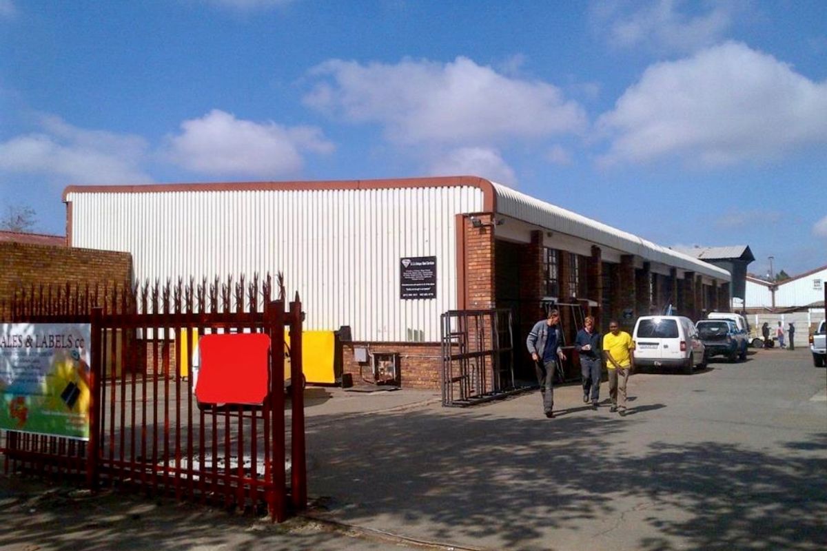 Industrial property exterior featuring corrugated metal cladding, brick masonry walls, and a paved driveway with secure perimeter fencing.