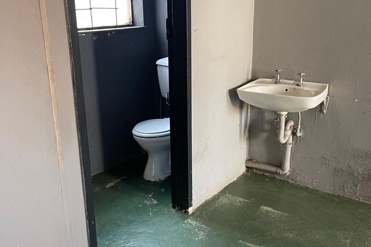A basic industrial-style bathroom featuring a wall-mounted basin and toilet, with worn concrete flooring and walls requiring cosmetic refurbishment.