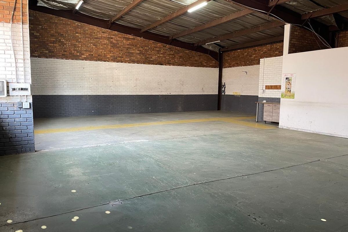 Spacious industrial utility area featuring exposed brick walls, concrete flooring, and high-clearance steel roof trusses, suitable for workshop or storage use.