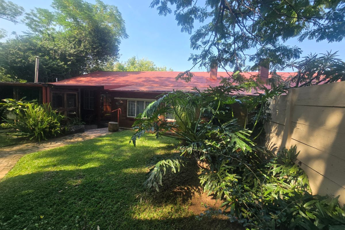 Rear view of a single-story house featuring a red corrugated metal roof, brick exterior, and a private garden with a paved walkway.