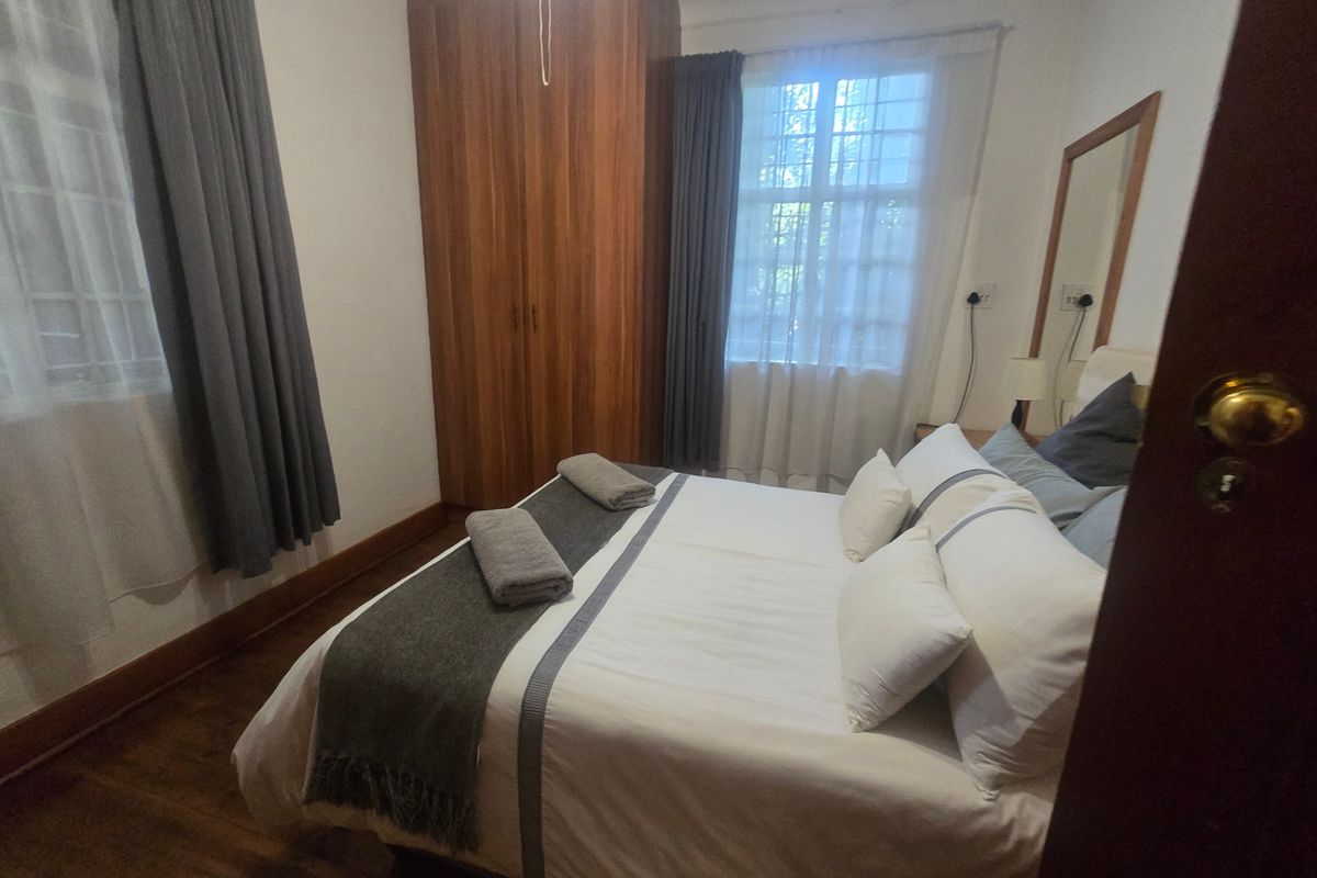 A cozy bedroom featuring timber flooring, a built-in wooden wardrobe, and windows fitted with security bars.
