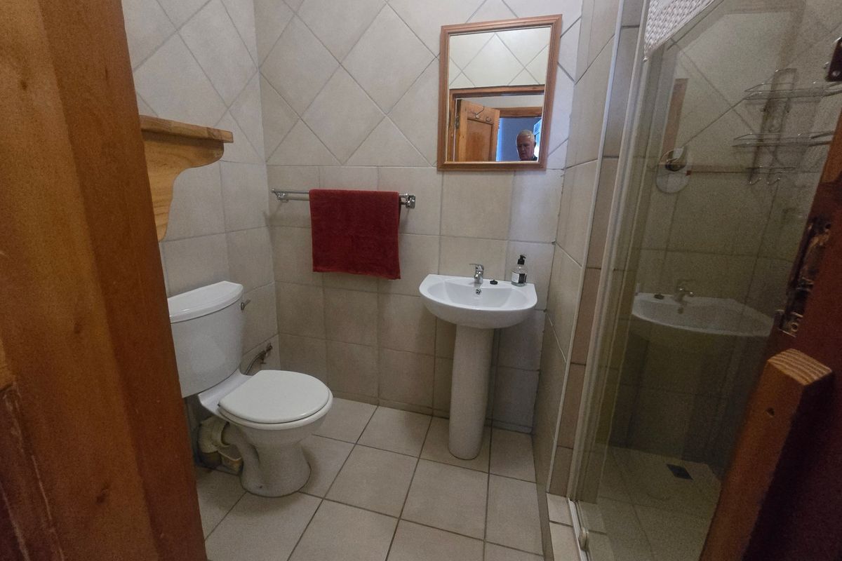 A functional bathroom featuring a pedestal basin, toilet, and a glass-enclosed shower with neutral wall and floor tiling.