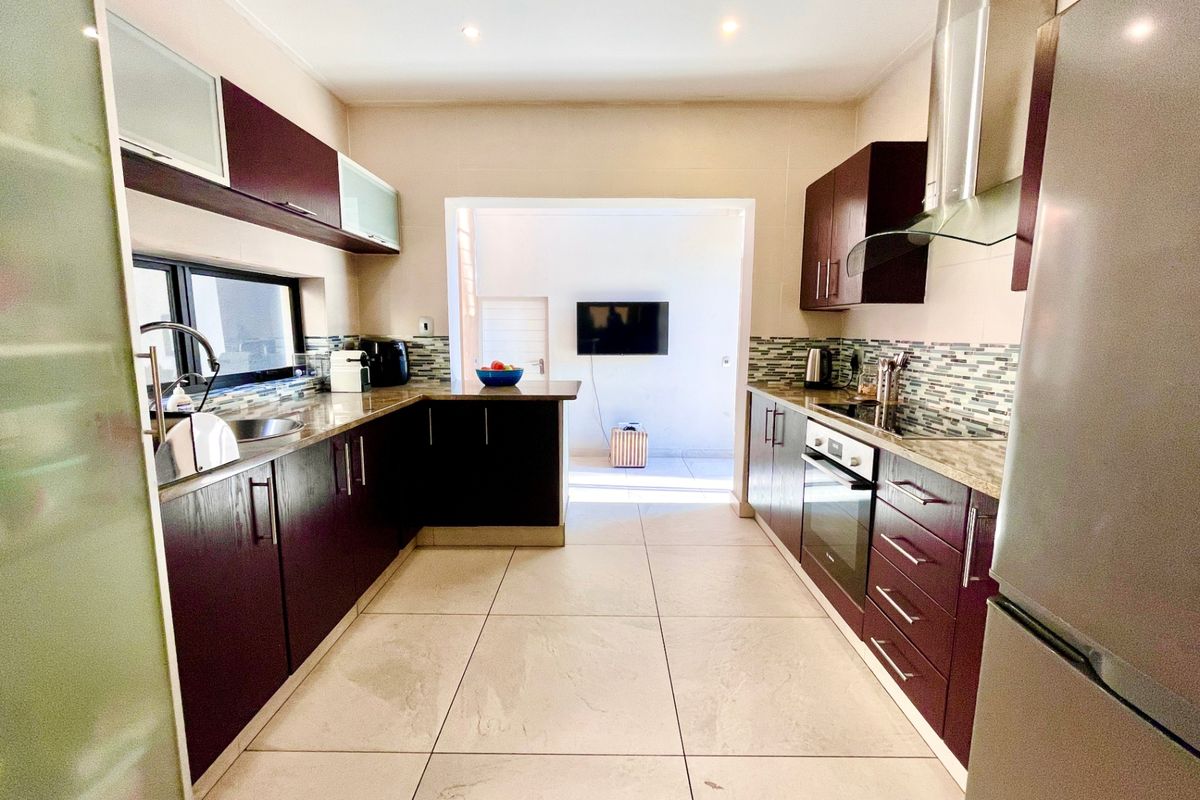 Modern kitchen featuring dark wood cabinetry, granite countertops, integrated stainless steel appliances, and tiled flooring, leading into an adjacent living area.