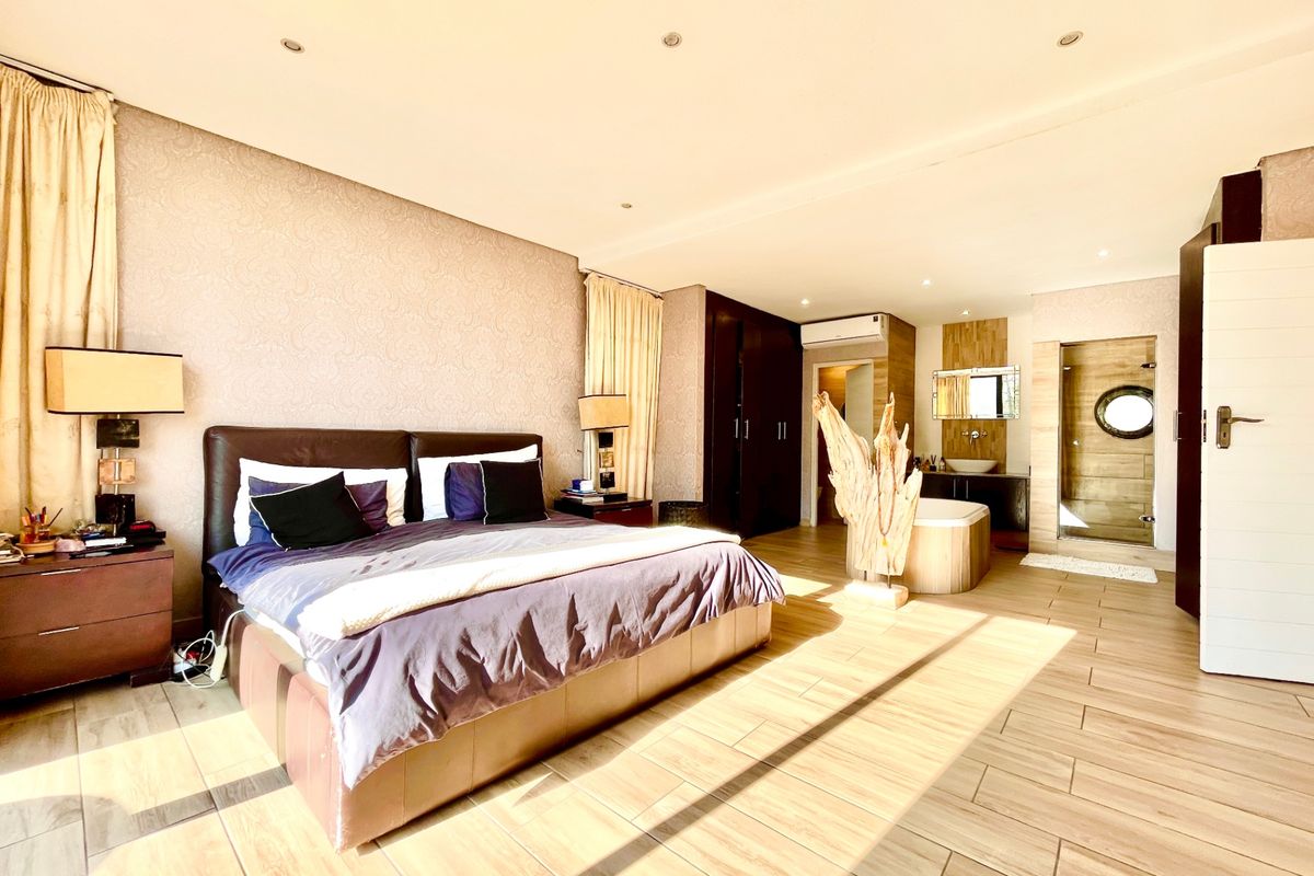 Spacious master bedroom featuring an open-plan en-suite bathroom with a freestanding tub, glass shower, vanity, built-in cupboards, and modern tiled flooring.