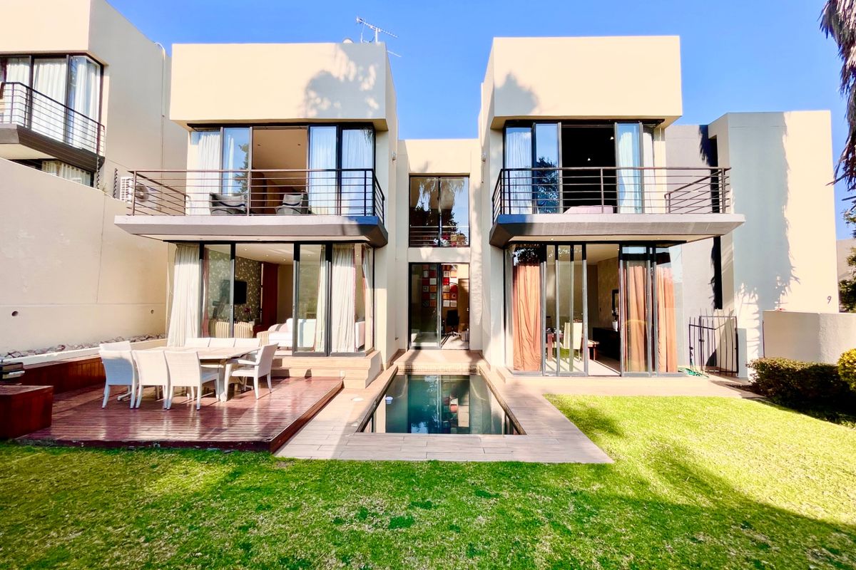 Rear view of a modern townhouse featuring a swimming pool, timber deck, and upper-level balconies with large sliding glass doors.