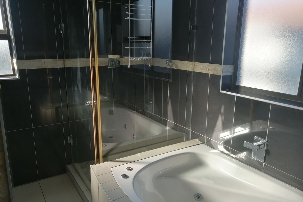 Modern bathroom featuring dark tiled walls, a built-in jet bathtub, and a separate glass-enclosed shower with chrome fixtures.