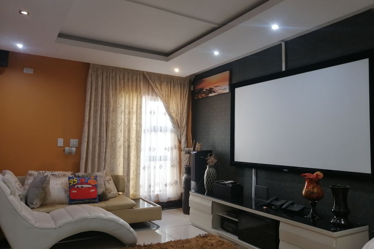 A comfortable living room featuring a dropped ceiling with recessed lighting, tiled floors, and a large wall-mounted projection screen for home entertainment.