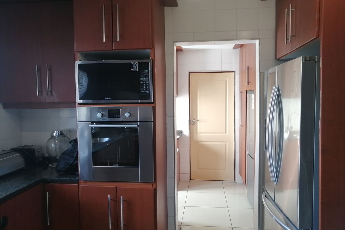 A functional kitchen featuring dark wood-look cabinetry, granite countertops, built-in oven and microwave, with a tiled backsplash and floor leading to a secondary area.